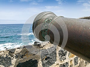 Closeup image of decorated muzzle of bronze cannon at old stone fortress walls at ocean