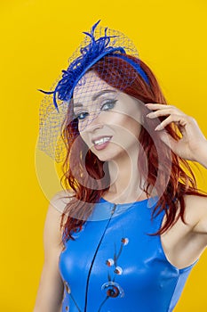 Closeup Image of Extravagant Caucasian Red-Haired Woman in Blue Artistic Dance Suit Posing In Shawl Hat On Yellow Background