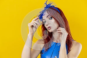 Closeup Image of Extravagant Caucasian Red-Haired Woman in Blue Artistic Dance Suit Posing In Shawl Hat On Yellow Background