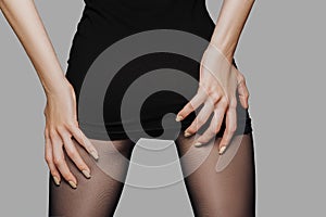 Cropped picture of female back in short black dress with hands on her buttocks. Lifting dress