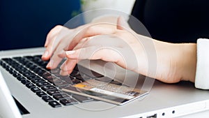 Closeup photo of female hands typing on keyboard. Credit card lying on laptop