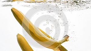 Closeup photo of fresh ripe yellow bananas falling and splashing in clear water against isolated white backgorund