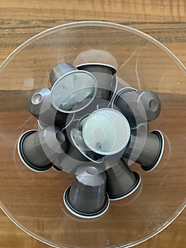 Closeup image of a glass holder filled with coffee capsules against a wooden background