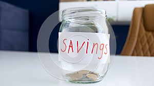 Closeup image of glass jar for money savings with few coins on white wooden desk