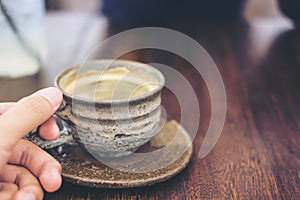 Closeup image of a hand holding clay mug of hot coffee on vintage wooden table