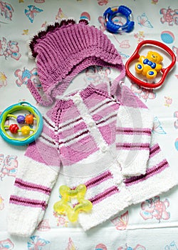 Closeup image of hand knitted child's hat & cardigan surrounded with toys on light copy space background