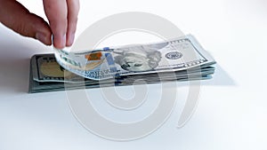 Closeup image of hand taking money from big stack of US dollars on white background