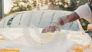 Closeup image of hand of young African man with yellow sponge washing headlight of his car at a self-serve car wash