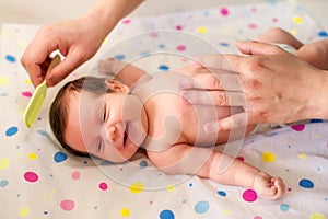 Closeup image: hands of dad combing laughing infant child. Newborn baby girl laying on blanket while father is brushing her hair