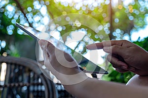 Hands holding and pointing at a black tablet pc screen with blur green background