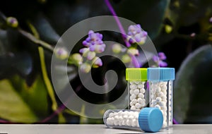 Closeup image of homeopathic medicine consisting of the pills bottle with blurred purple flowers and green leaves background