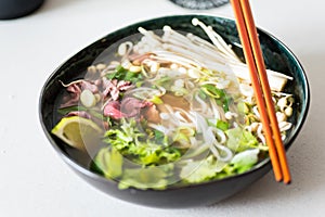 Closeup image of hot soup Pho Bo in a dark bowl