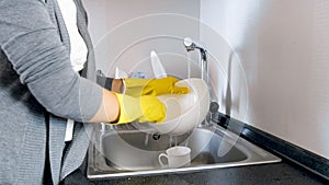 Closeup image of housewife in yellow protective gloves washing dishes in sink