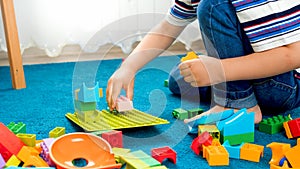 Closeup image of little boy sitting on floor and playing with toy blocks