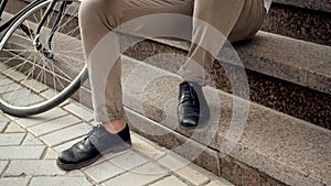 Closeup photo of male feet sitting on stone stairs next to bicycle