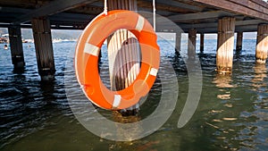 Closeup image of orange life saving ring hanging on wooden pier at sea beach