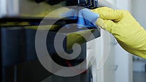 Closeup Image with Person Hands Wearing Protective Yellow Household Gloves in the Kitchen and Cleaning a Stove