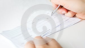 Closeup image of person writing bank cheque for charity purposes