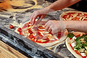 Closeup image of pizzamaker spreading pepperoni on pizza dough
