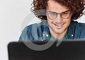 Closeup image of positive young man smiling and sitting at his desk with laptop chatting online with friends.