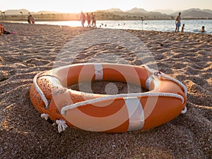 Closeup image of red plastic life saving ring on sandy sea beach at sunset light