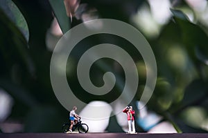 Small photographer and bicycle rider model figures on wooden floor with blur green nature background