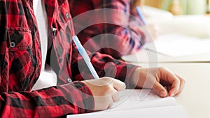 Closeup image of teenage girl holding pen and writing homework