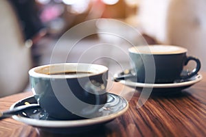 Closeup image of two blue cups of hot latte coffee and Americano coffee on vintage wooden table