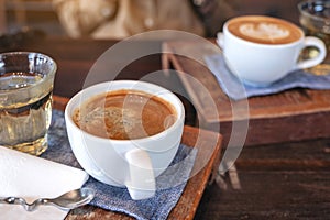 Two white cups of hot coffee and a glass of tea on vintage wooden table in cafe