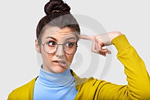 Closeup image of uncertain young woman with a bun hairstyle, bitting her lips, being doubtful, wearing casual outfit, spectacles