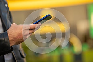 Closeup image of an unrecognizable young man holding mobile phone in hand, blurred background