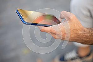 Closeup image of an unrecognizable young man holding mobile phone in hand, blurred background