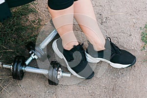 Closeup image of a woman legs in black sneakers near dumbbells outdoor on ground