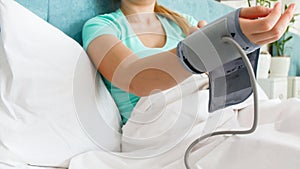 Closeup image of woman lying in bed and wearing digital blood pressure manometer sleeve on hand