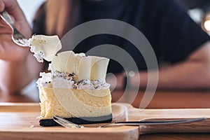 Closeup image of a woman`s hand cutting white chocolate cheese cake with fork on wooden plate