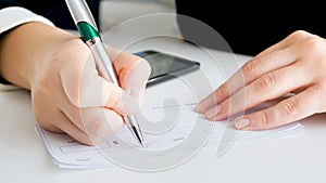 Closeup image of woman writing signature on banking cheque