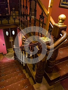 Closeup image of wooden staricase with red carpet and carved handrails at old hotel or restaurant
