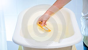 Closeup image of young mother checking water temperature in baby bathtub with thermometer