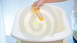 Closeup image of young woman checking water temperature with thermometer in baby bathtub