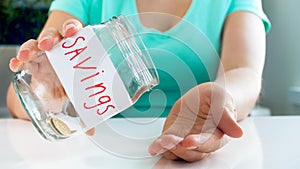 Closeup photo of young woman having financial problems emptying glass jar with money savings