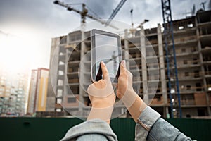 Closeup image of young woman using diigatl tablet aginst building under construction