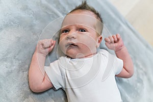 Closeup indoor portrait of a european infant baby boy in light blue bodysuit clenching his fists and giving a surprised