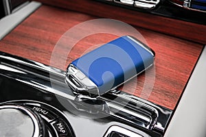 Closeup inside vehicle of wireless blue leather key ignition on natural wood panel. Wireless start engine key. Car key remote isol