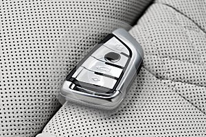 Closeup inside vehicle of wireless key ignition on white perforated leather seat. Wireless start engine key. Car key remote isolat