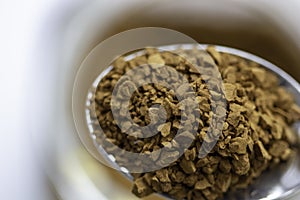 Closeup of instant coffee grains in the spoon with a cup on the blurred background