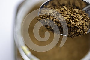 Closeup of instant coffee grains in the spoon with a cup on the blurred background