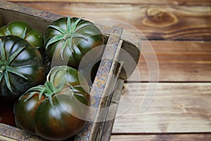 Closeup of isolated group dark black beef cabomar tomatoes in rustic wood box, brown wooden planks background