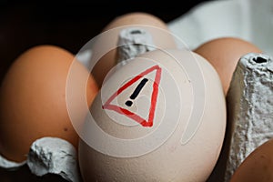 Closeup of isolated raw brown eggs in carton box with warning sign - salmonella infection risk and cholesterol consumption concept