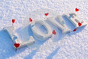 Closeup of Isolated Word & x22;Love& x22; from Wooden Pieces in the Snow on Sunny Winter Day with White Background with Red Heart