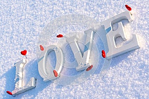 Closeup of Isolated Word & x22;Love& x22; from Wooden Pieces in the Snow on Sunny Winter Day with White Background with Red Heart